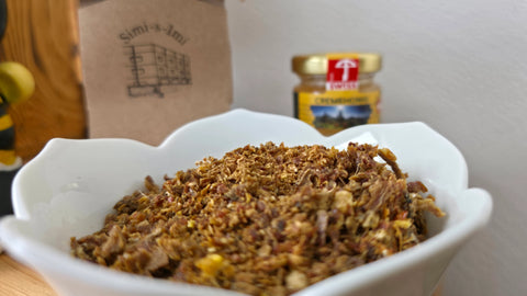 Grob zerkleinerte Rohpropolis in einer weißen Schale, im Hintergrund unscharf ein Honigglas und eine Verpackung mit der Aufschrift simi-s-imi