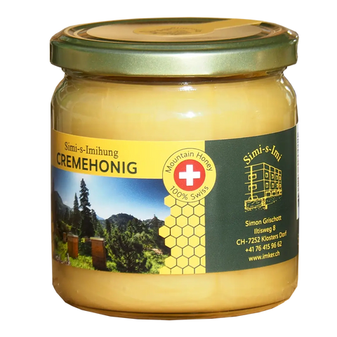 Ein Glas mit Simi-s-Imihung Berg-Cremehonig mit goldenem Deckel. Das Etikett zeigt eine Schweizer Flagge, eine malerische Berglandschaft, ein Wabenmuster und Kontaktdaten. Der Honig im Inneren ist hellgelb und cremig. Ausgezeichnet mit dem Schweizer Qualit 100% Swiss Mountain Honey