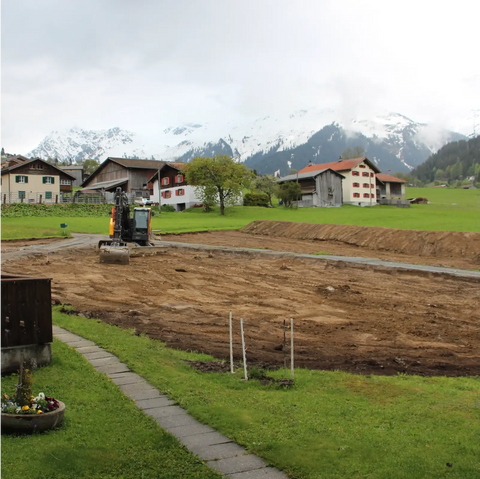 Beginn der Bauarbeiten für das neue Ökonomiegebäude der Imkerei in Klosters, 2019 – Aushubarbeiten auf dem Baugrundstück vor alpiner Kulisse.